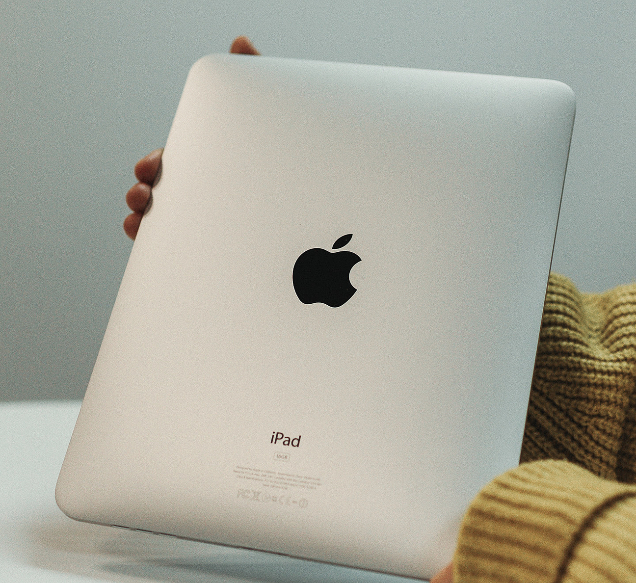 ein iPad wird in zwei Händen gehalten, auf der silbernen Rückseite ist das schwarze Apple Logo zu sehen