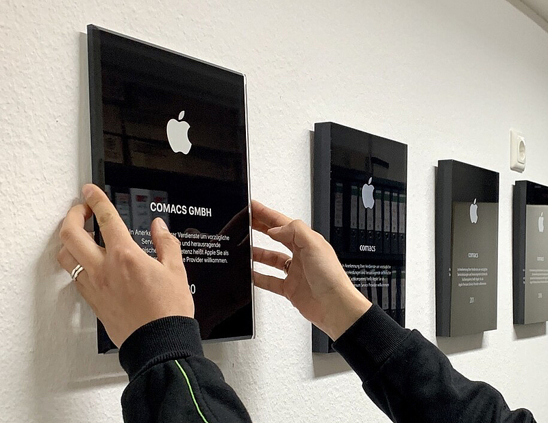 zwei Hände hängen eine schwarze Plakette an die Wand, in einer Reihe mit anderen