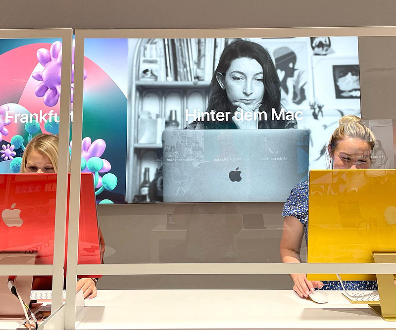 zwei Personen arbeiten im Stehen hinter zwei iMacs, man sieht nur ihre Augen