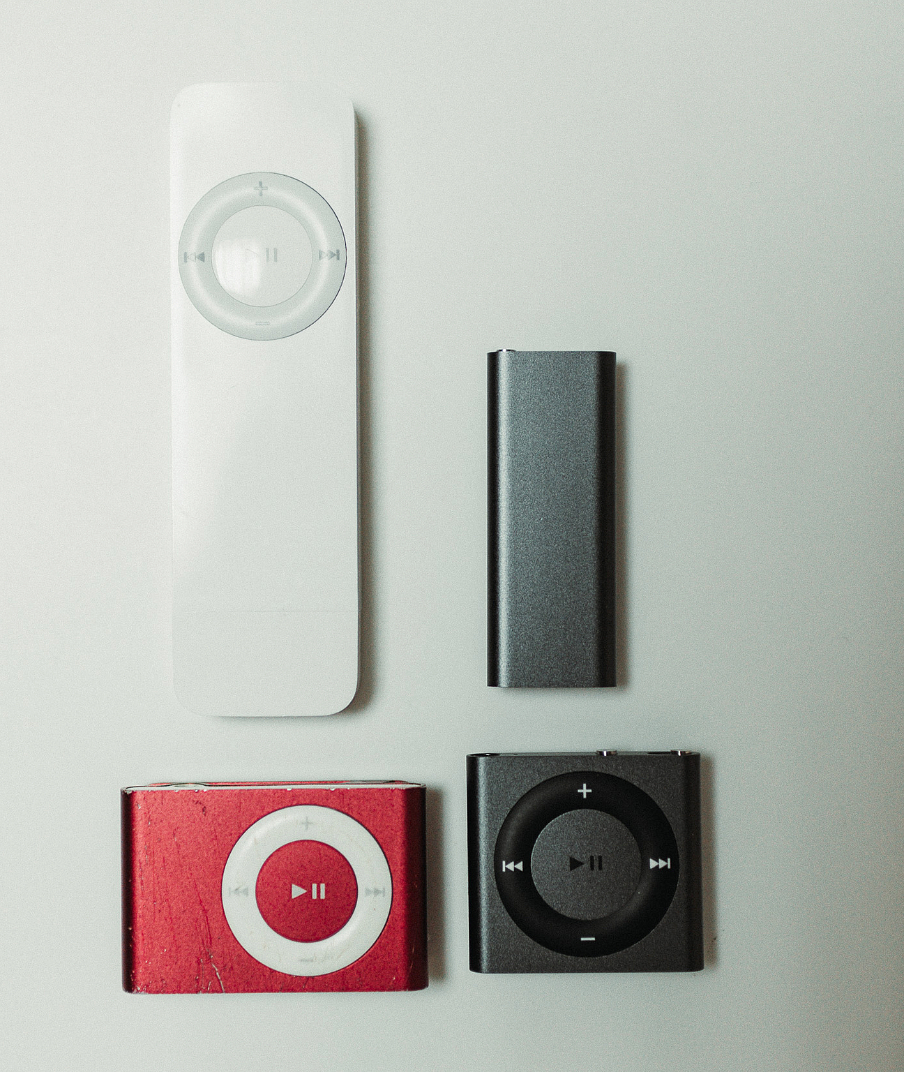 iPod shuffle family: 1. Generation in weiß, 2. Generation rechteckig in rot. 3. Generation rechteckig in grau, 4. Generation viereckig in grau