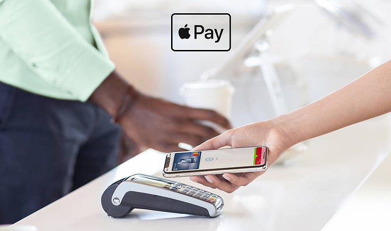 eine Hand hält ein iPhone an ein Kartenlesegerät um mit der Funktion ApplePay zu bezahlen