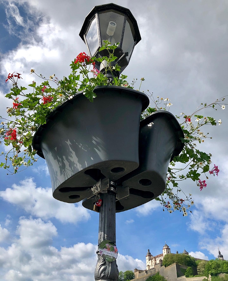 eine Blumenampel hängt an einer Laterne, im Hintergrund ist die Festung Marienberg zu sehen